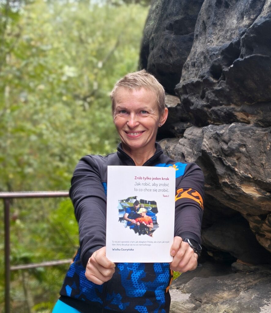 Autorka Wiolka Czuryńska w stroju sportowym prezentuje e-book „Zrób tylko jeden krok. Tom 1” na tle skał w Tiske Steny.