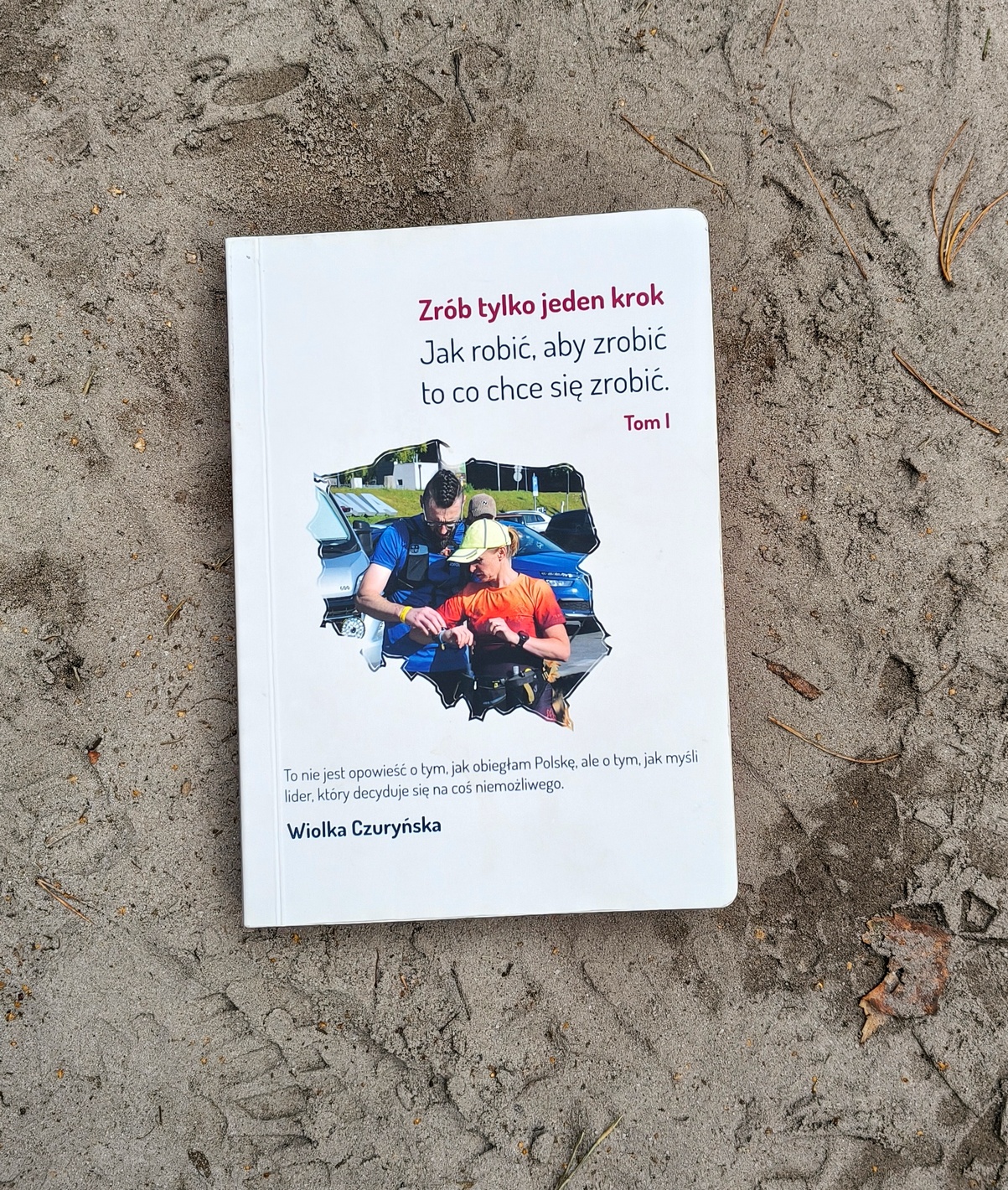 Przednia okładka papierowej wersji książki „Zrób tylko jeden krok” ułożona na piaszczystej ścieżce.