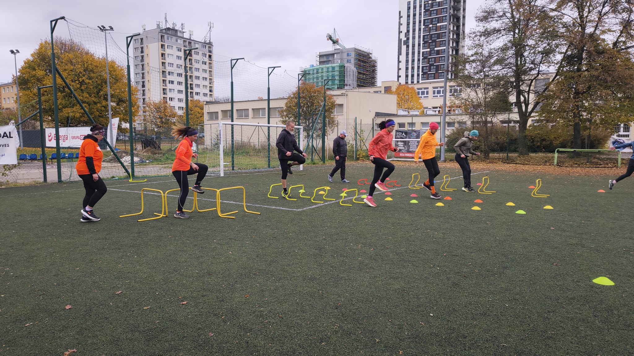 treningi biegowe Gdynia - trening techniki i rytmu biegu – zawodnicy pokonujący niskie płotki lekkoatletyczne na boisku zewnętrznym w Gdyni.